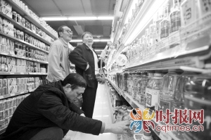 超市中的货架上摆放着各式各样的白酒,市民在货架前挑选